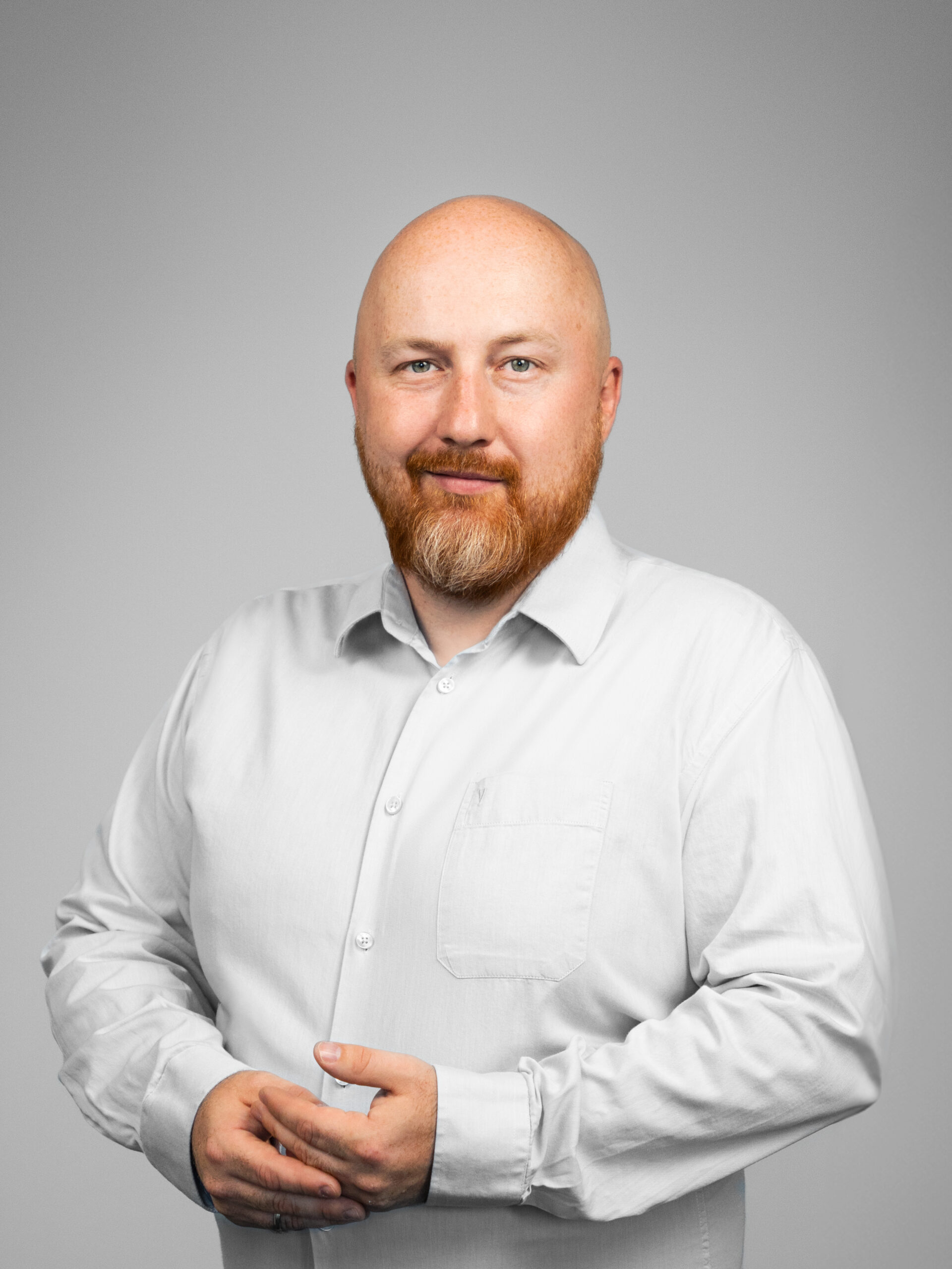 Portrait of Michał Szymański, Delivery Director at Espeo Software, a man with a bald head and reddish-brown beard, wearing a light-colored buttoned shirt, smiling at the camera.