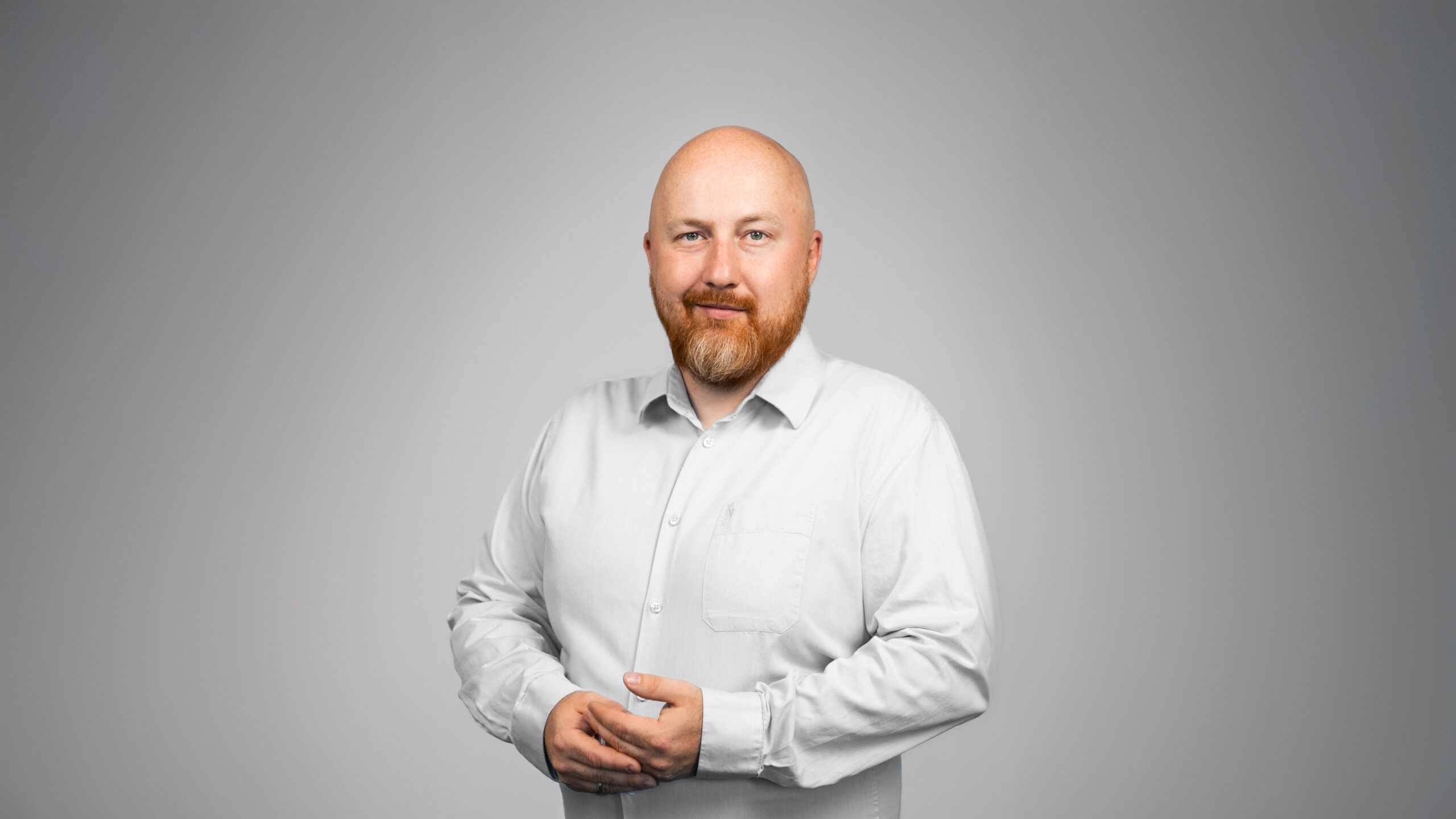 Portrait of Michał Szymański, Delivery Director at Espeo Software, a man with a bald head and reddish-brown beard, wearing a light-colored buttoned shirt, smiling at the camera.