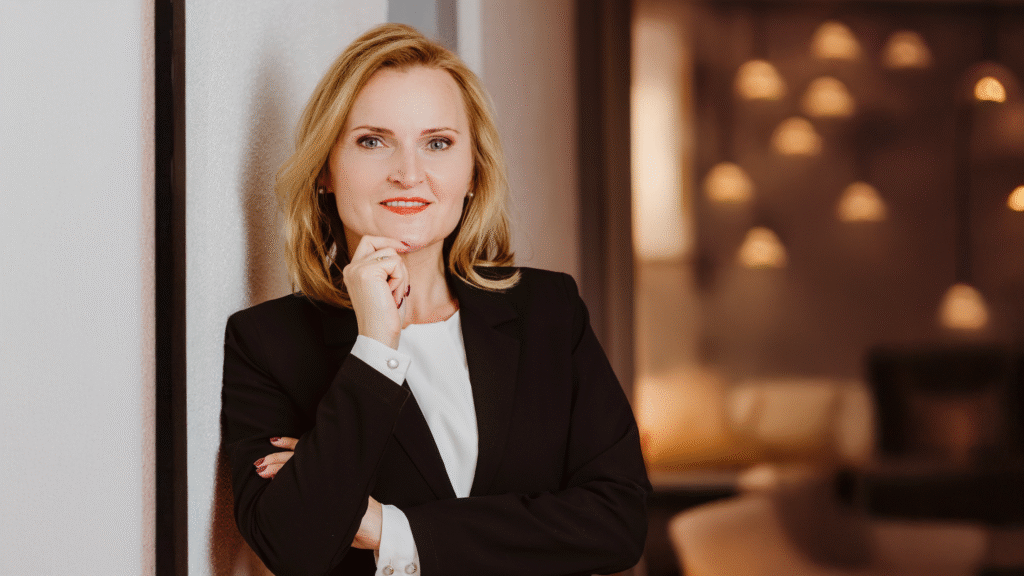 Portrait of Dr Katharina Lasota Heller, Managing Partner at Lex Legal Services, posing in a black blazer and white blouse, smiling confidently with her hand resting on her chin.