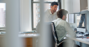 Man working at a computer in a modern office environment, focused on analysing information on screen.