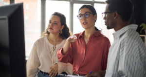 Three professionals collaborating while analysing information displayed on a large screen in an office.