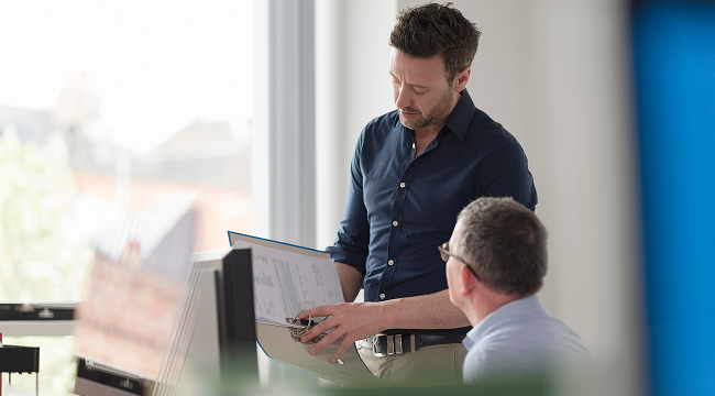 Three colleagues in a modern office reviewing information together on a tablet device.